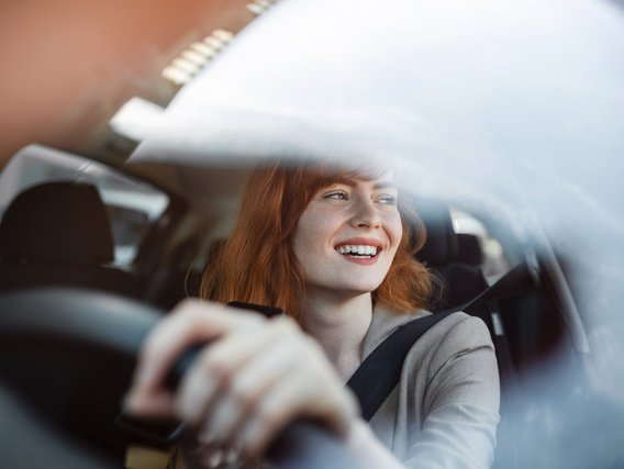 Frau fährt ein Auto, Hände am Lenkrad, durch die Windschutzscheibe gesehen.
